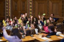 Mädchen im Parlament stimmen mit grünen Zettel ab, die sie in die Luft halten.